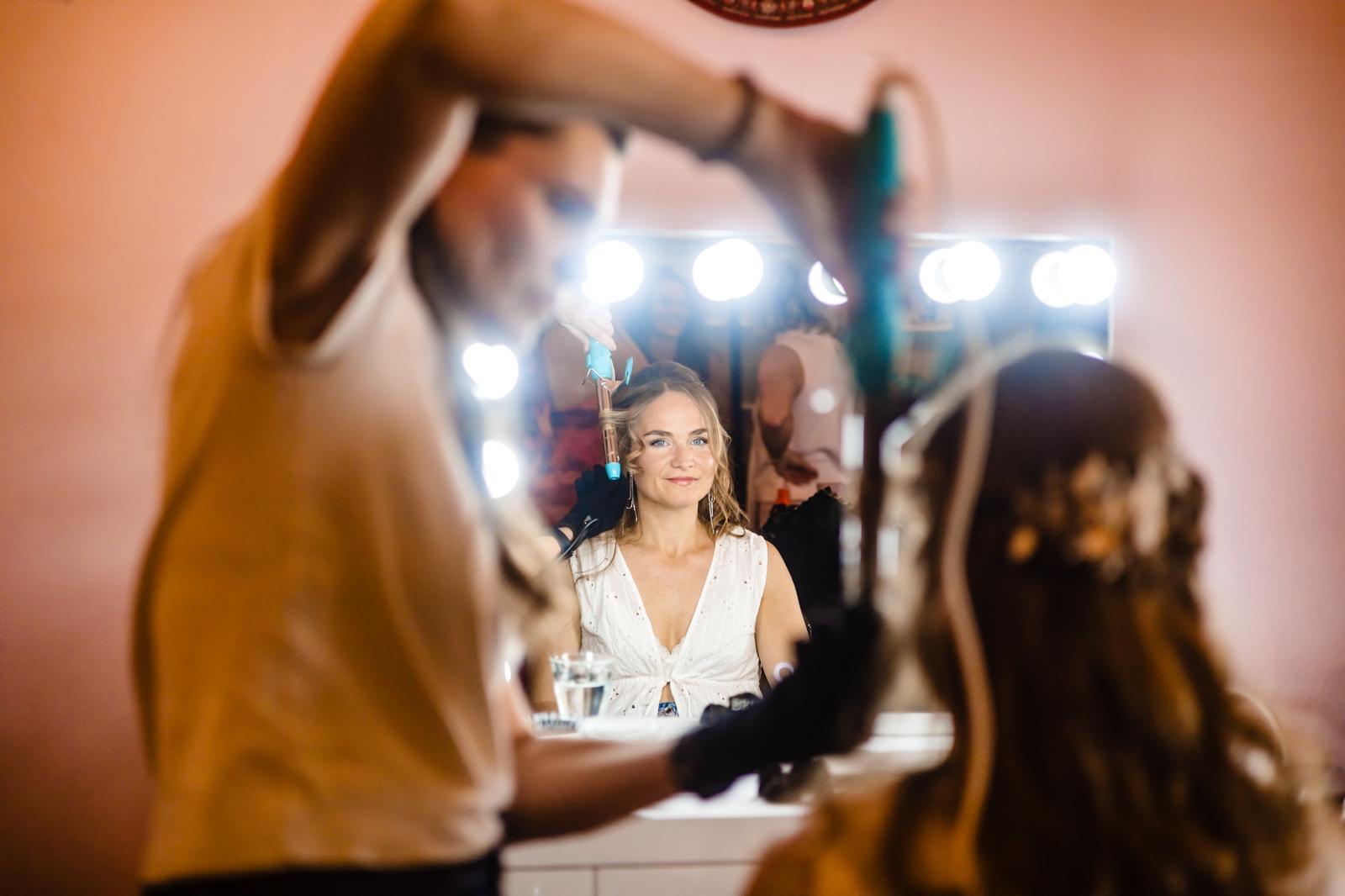 Bruid krijgt haar kapsel gestyled voor de trouwdag, weerspiegeld in de visagiespiegel
